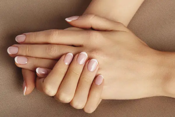 Dłonie z klasycznym francuskim manicure. Delikatny róż i biel na paznokciach, idealne dopełnienie naturalnego piękna. To kwintesencja manicure biologicznego.